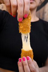 Woman stretching fried mozzarella cheese sticks.	