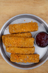 Gastronomy. Top view of fried mozzarella cheese fingers with a spicy dipping sauce, in a metal dish on the wooden table.
