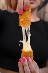 Woman stretching fried mozzarella cheese sticks.	

