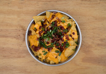 Nachos with cheddar background. Top view of nachos with cheddar cheese, green onion and crispy bacon in a metal dish on the wooden table.