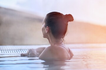 Woman enjoying view, relaxing in outdoor thermal pool on a winter day. Snowy mountains on the background.