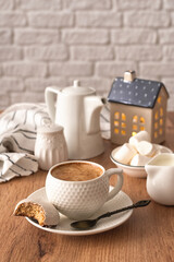 Winter composition on a wooden background. A cup of coffee, white glazed cookies, a creamer, a coffee pot and a decorative house on a wooden table. Cozy winter concept. Selective focus.