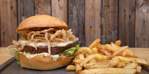 Plant based burger. Not Burger. Closeup view of NotCo hamburger with lettuce, crispy onion rings, cheese, NotCo mayo and french fries, in a metal dish with a wooden background.