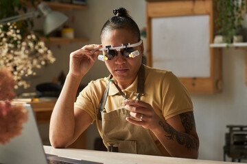 Portrait of artisanal jeweler wearing magnifying glasses while working on art piece