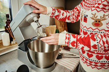 Woman in festive christmas sweater preparing dough for cookies at home kitchen. Female hands use...