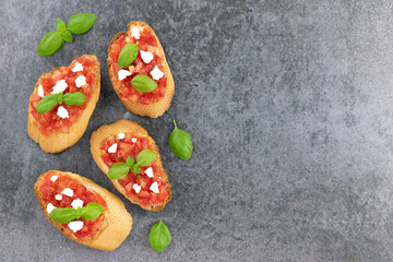Slices of Italian tomato bruschetta or crostini with fresh basil on a gray background, top view. Italian appetizers. Copy Space.