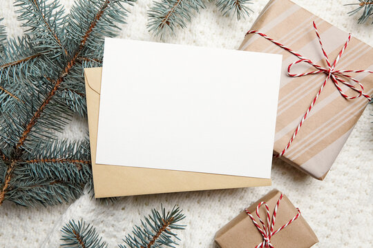 Christmas greeting card mockup with gift box and fir tree branches on white knitted pullover background, top view, flat lay