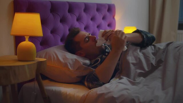 Unwell man sneezing in bed feeling sick. Realtime