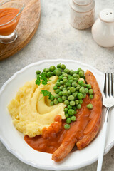 Bangers and mash. Grilled sausages with mash potato and green pea on white plate on grey background. Traditional dish of Great Britain and Ireland. BBQ beef sausages. Top view.