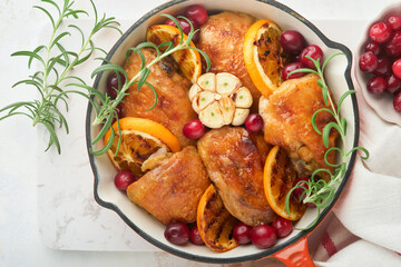 Baked chicken thighs with orange, cranberry and spicy herbs rosemary servered in frying pan on light background. Festive Christmas Dinner Concept menu. Top view. copy space