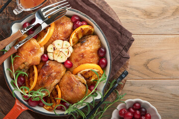 Baked chicken thighs with orange, cranberry and spicy herbs rosemary servered in frying pan on light wooden rustic background. Festive Christmas Dinner Concept menu. Top view. copy space