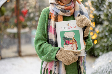 Woman holding magazine with New Year's cover at snowy backyard decorated for a winter holidays....