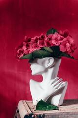 Fresh bunch of colorful hydrangea in vase in shape of womens face. Trendy Ceramic Vase of human head, Handmade Modern Statue Art Flower Vase. Toned in viva magenta color of the year 2023