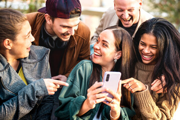 Multicultural young people having fun with mobile phone at urban city yard - Happy guys and girls spending time together sharing funny content online on smartphone social networks - Bright warm filter