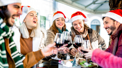 Trendy young people on santa hat celebrating Christmas with red wine at food street market - Winter friendship concept with friends enjoying time and having fun eating together - Bright vivid filter