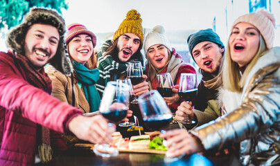 Young trendy friends toasting red wine at restaurant garden out side - Life style concept with mixed happy people having fun together at winery bar eatery wearing winter clothes - Viva magenta filter