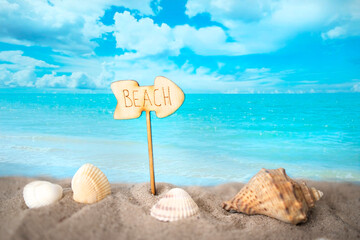 Fototapeta na wymiar Summer beach with shells and wooden sign. Blur azure sea on background.