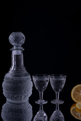 decanter of vodka with shot glasses, lemon on black background