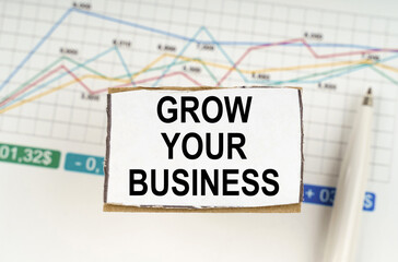 Against the background of business graphics and pens, a sign with the inscription - Grow your business