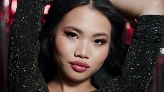 Alluring glamour asian woman with sensual look posing to a camera over red shiny background. Close up. 
