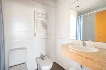Interior of white tiled bathroom with toilet, bidet, radiator and shower curtain in reflection of mirror