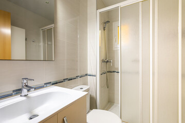 Interior of modern tiled bathroom with white sink, wooden furniture, mirror and shower cabin.