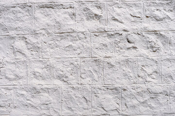 Background of white cracked plaster on the wall. An old wall with uneven cladding is full of cracks and roughness. Rough background of a white wall with bumps. Free space for text or advertisement