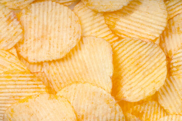 Yellow crispy ridged potato chips close up. Food background, banner, header, wallpaper.