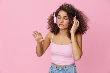 Happy woman wearing headphones with curly hair listening to music and singing along with her eyes...