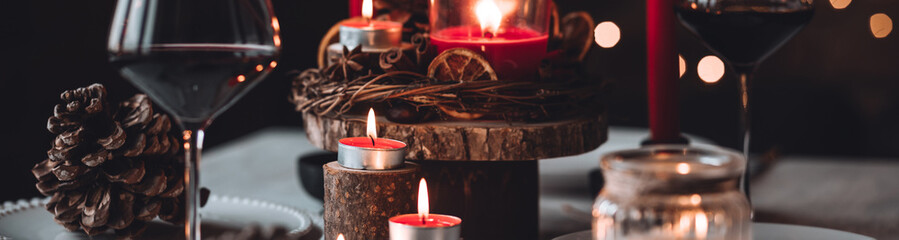 Rustic table decor for Christmas or New Year family dinner. Centrepiece with red candle, dry orange, cone, cinnamon, anise. Zero waste eco-friendly home. Cozy atmosphere, dark background. Banner