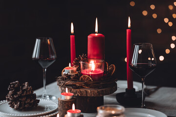 Rustic table decor for Christmas or New Year family dinner. Centrepiece with red candle, dry orange, cone, cinnamon, anise. Zero waste eco-friendly home. Cozy atmosphere, dark background. Close up