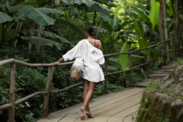 Naklejka na ściany i meble Young woman walking in green tropical park, back view