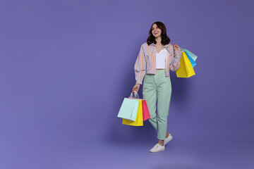 Beautiful young woman with paper shopping bags on purple background