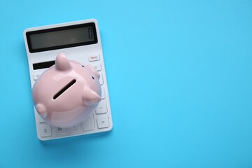 Piggy bank and calculator on light blue background, top view. Space for text