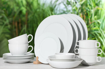 Set of clean dishware on white table against blurred background