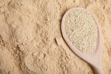Spoon with sesame seeds on flour, top view. Space for text