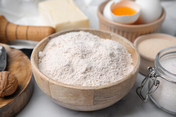 Fototapeta na wymiar Bowl of flour and other ingredients on white table, closeup