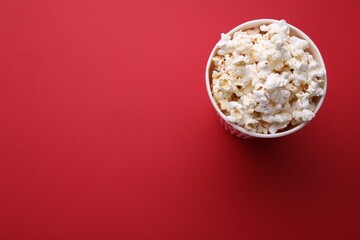 Paper bucket with delicious popcorn on red background, top view. Space for text