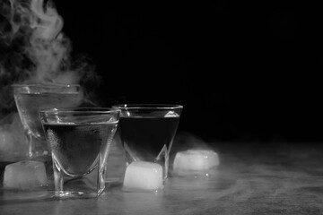 Vodka in shot glasses with ice on table against black background, space for text - obrazy, fototapety, plakaty