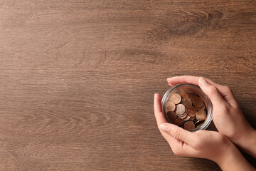 Woman holding glass jar with coins on wooden table, closeup. Space for text