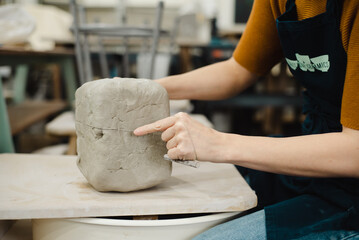 Side view of potter hands sectioning clay with wire cutter on wooden board in ceramic pottery studio