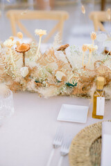 Wedding table setting with dry beige decorative flowers and white tablecloth prepared for guests