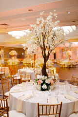 Front view of beautiful decorative tree with fresh flowers, placed on festive table with setting and crystal during wedding ceremony in restaurant