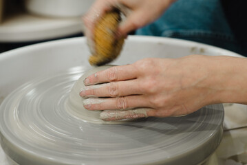 Closeup of potter hands working on pottery wheel in ceramic studio with clay hands side view with pottery wheel in motion