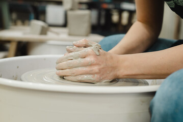 Closeup of potter hands working on pottery wheel in ceramic studio with clay hands side view with pottery wheel in motion