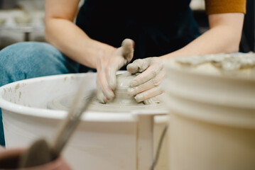 Closeup of potter hands working on pottery wheel in ceramic studio with clay hands front view with pottery wheel in motion