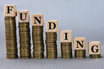 FUNDING - word on a wooden cubes against the background of stacks of coins