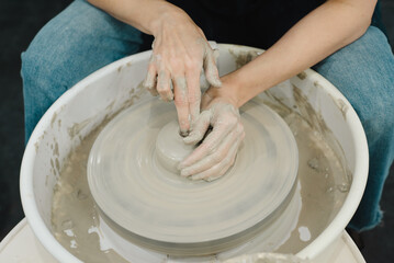 Closeup of potter hands working on pottery wheel in ceramic studio with clay hands front top view with pottery wheel in motion