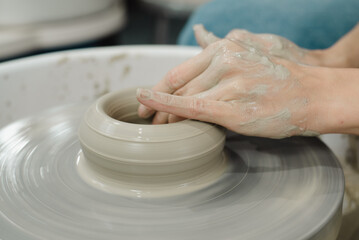 Closeup of potter hands working on pottery wheel in ceramic studio with clay hands side view