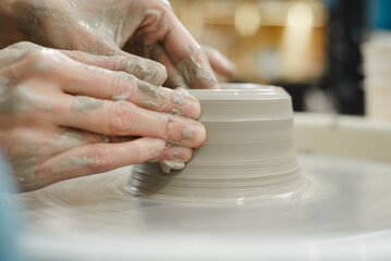 Closeup of potter hands working on pottery wheel in ceramic studio with clay hands side view